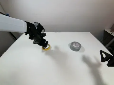 Robot gripper positioned around the yellow tape roll before grasping